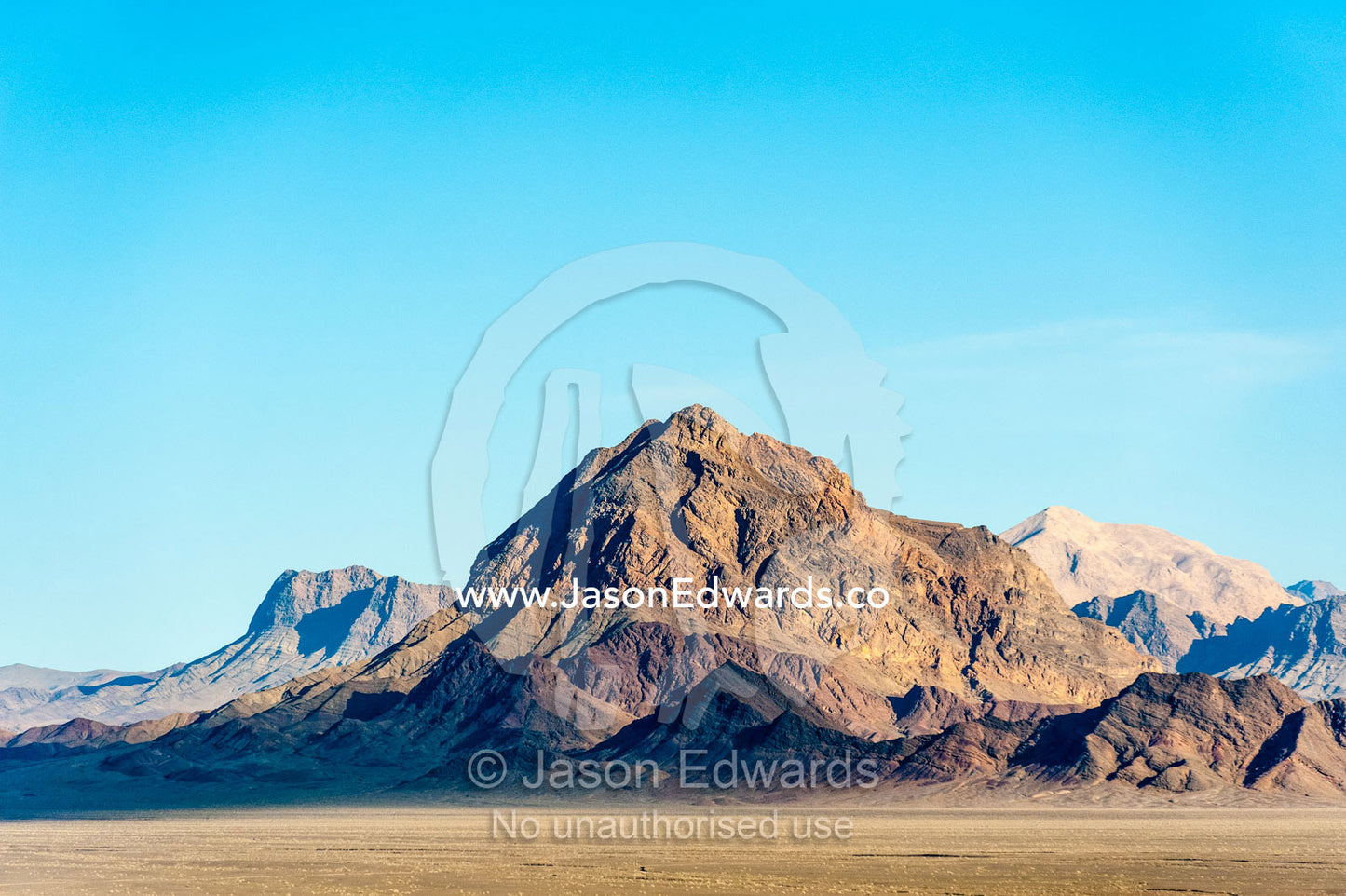 Jagged desert mountains scoured by erosion rise from a desert plain. Kharanagh, Yazd, Yazd Province, Islamic Republic of Iran.