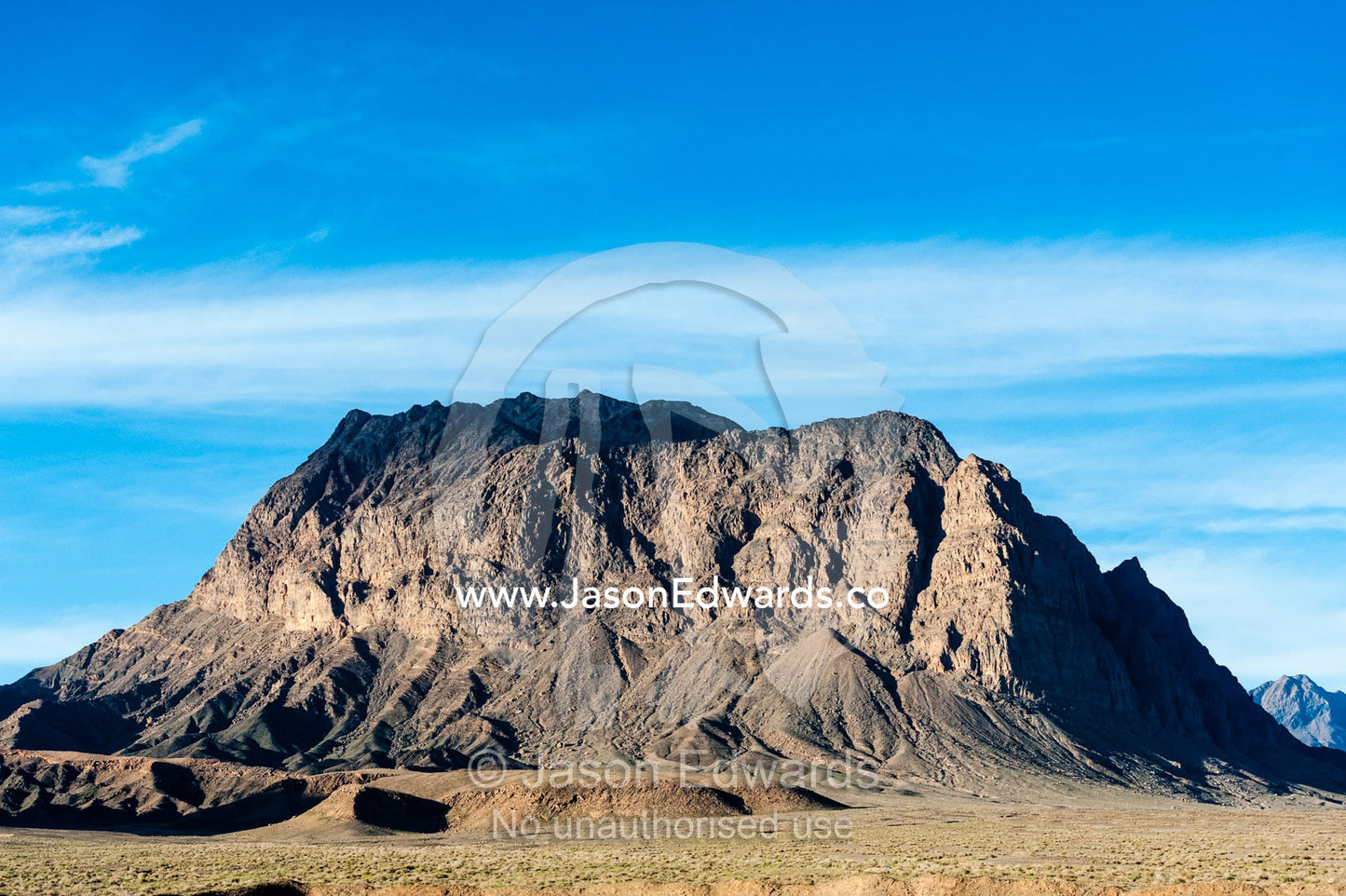 Jagged desert mountains scoured by erosion rise from a desert plain. Kharanagh, Yazd, Yazd Province, Islamic Republic of Iran.