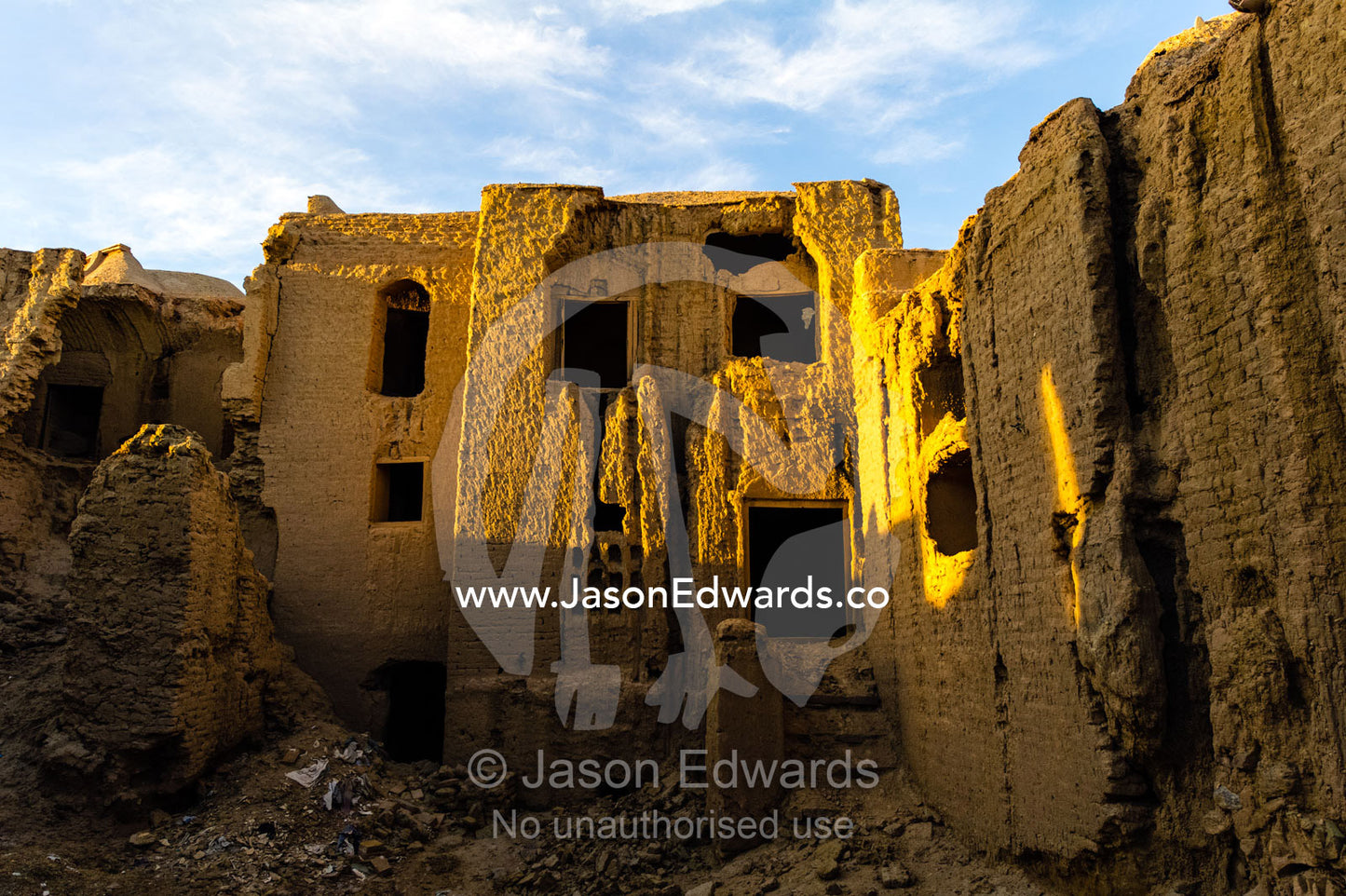 Sunset warms buildings of crumbling handmade brick ruins of an ancient abandoned village in the desert. Kharanagh, Yazd, Yazd Province, Islamic Republic of Iran.