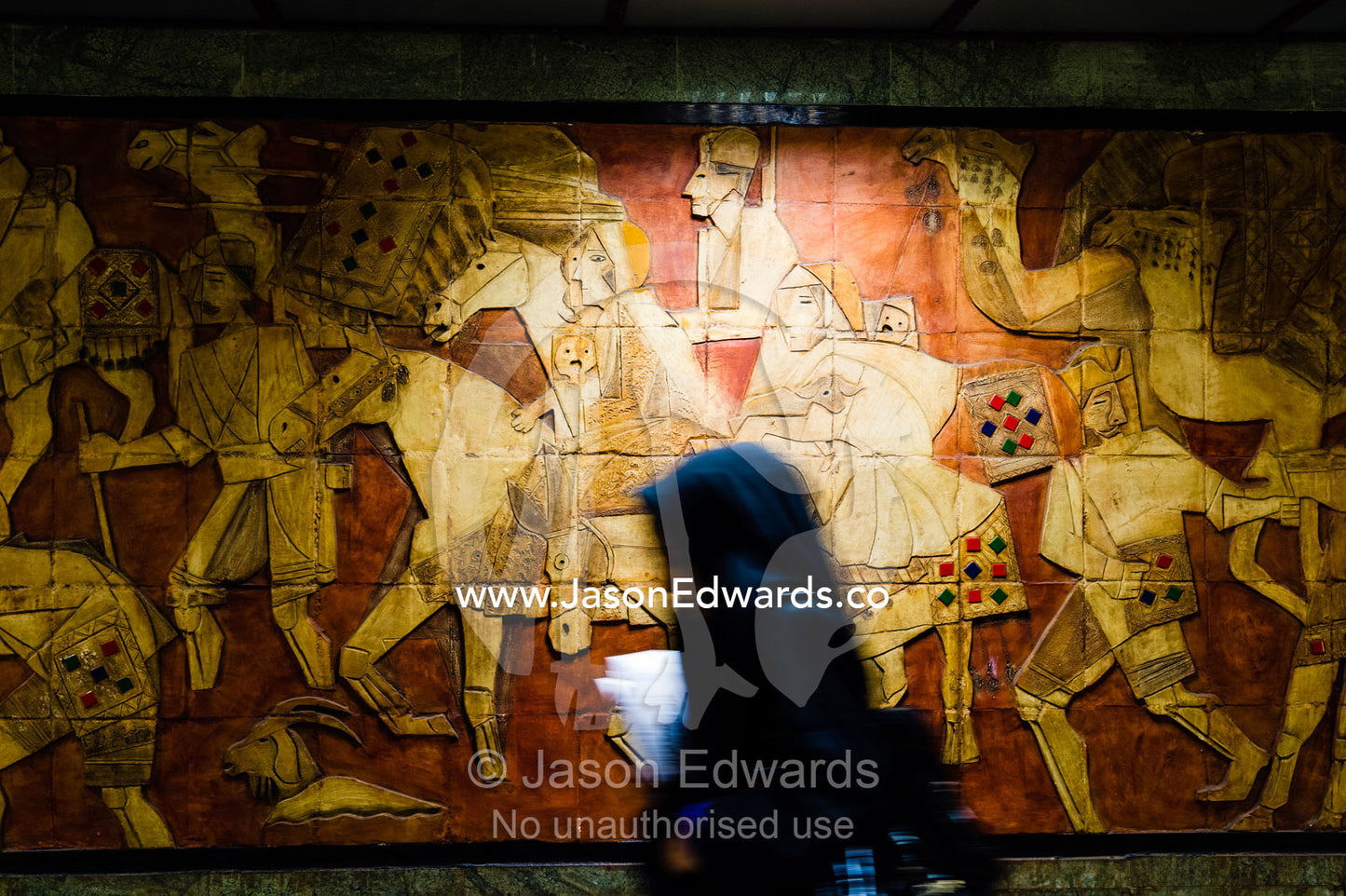 A woman walks past a frieze featuring Persian art in a railway subway system beneath Tehran. Tehran, Tehran Province, Islamic Republic of Iran.