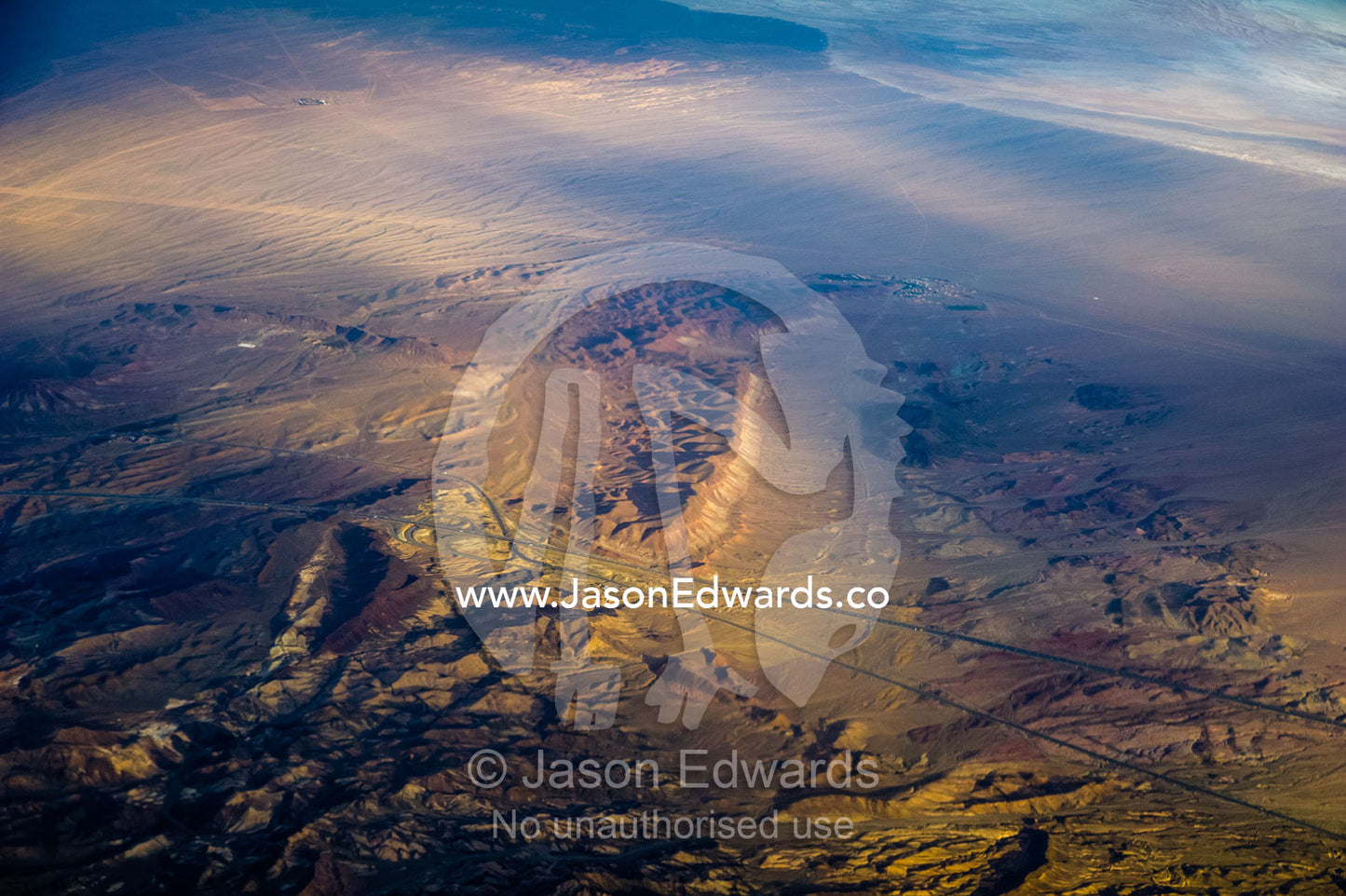A high altitude view of sunrays lighting a road passing through jagged mountain peaks in the desert. Islamic Republic of Iran.