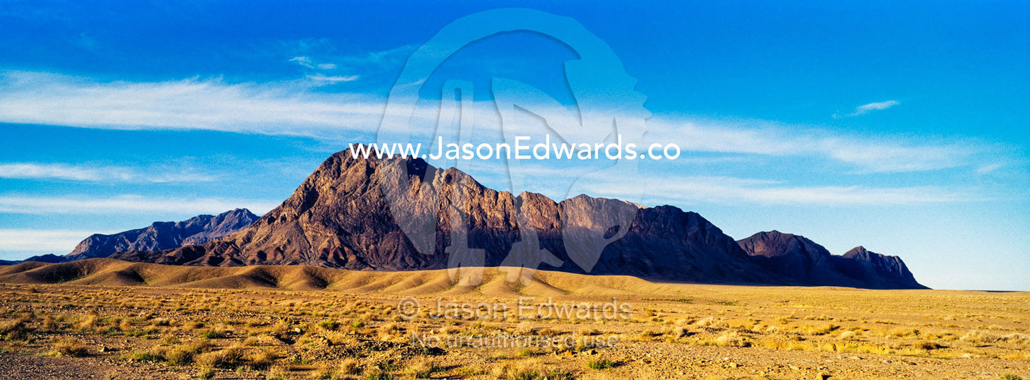 Jagged desert mountains scoured by erosion rise from a desert plain. Kharanagh, Yazd, Yazd Province, Islamic Republic of Iran.