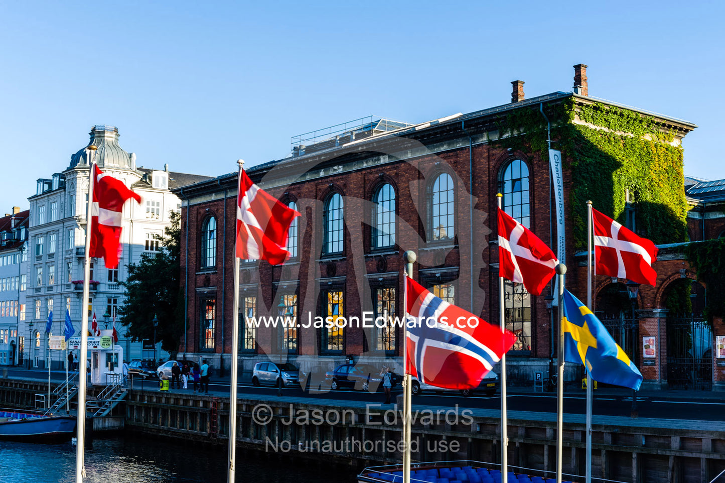 Danish flags fluttering in the wind by a canal. Nyhavn Canal, Copenhagen, Hovedstaden Region, Denmark.