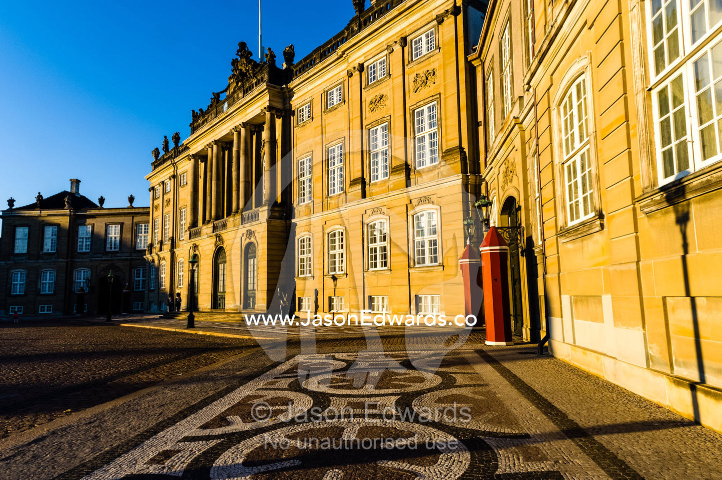 Sunset falls across the facade of the Royal Palace and it's cobblestone courtyard and guard post. Amalienborg Palace, Copenhagen, Denmark.