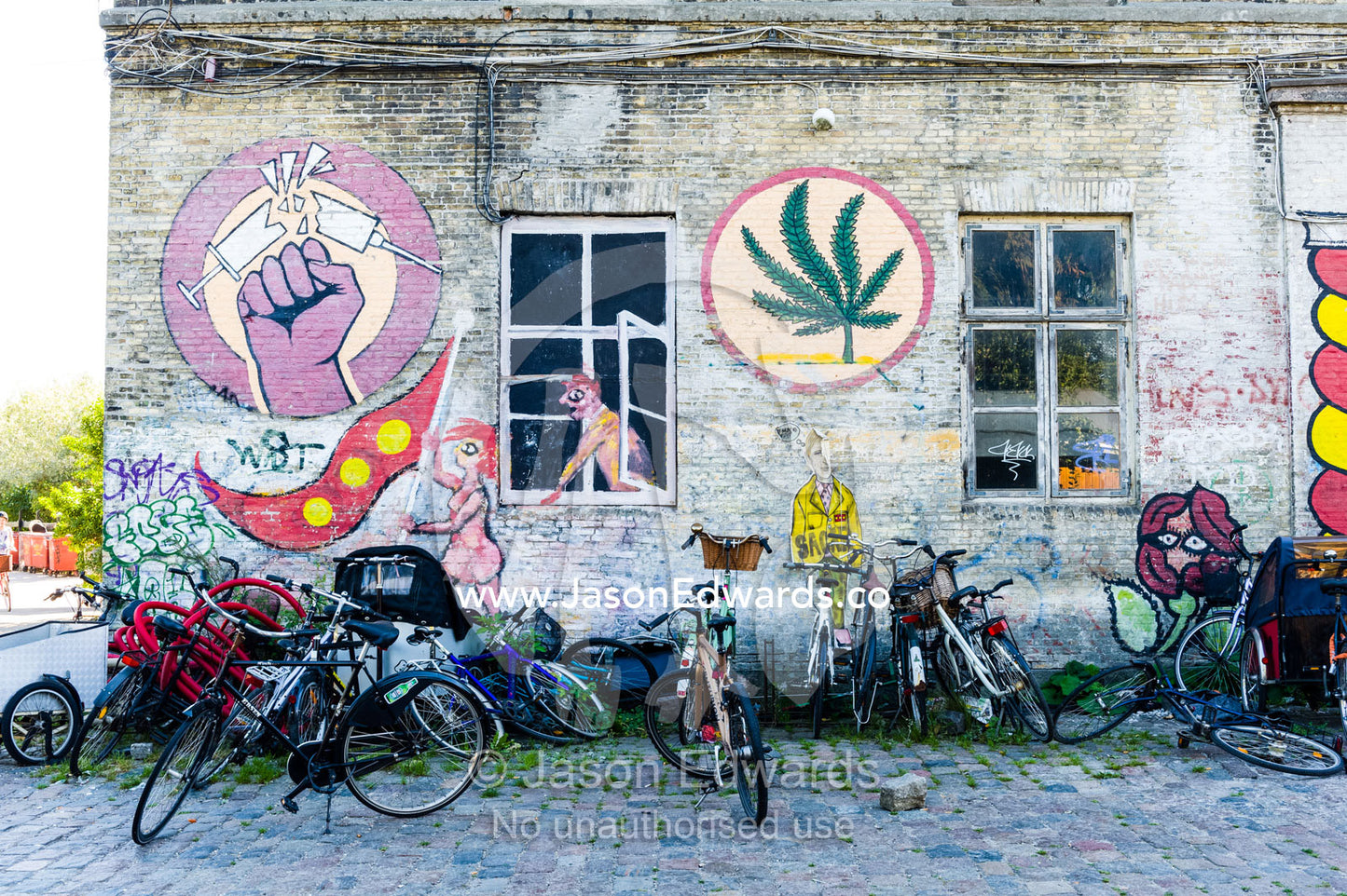 Bicycles parked by a wall covered in street art featuring drug themes. Christiania, Freetown Christiania, Christianshavn, Copenhagen, Denmark.