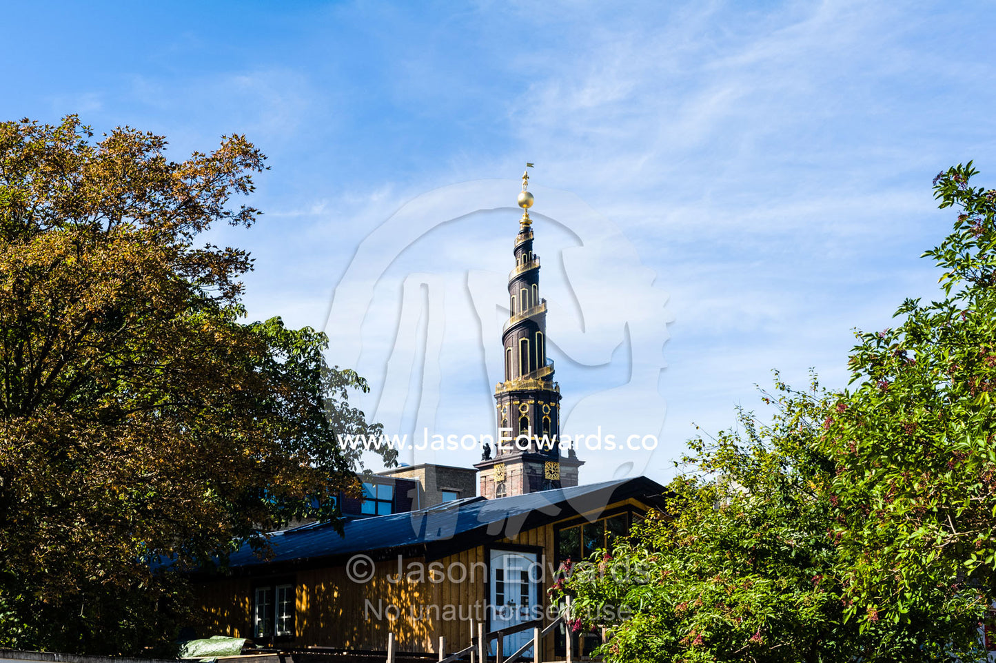 The spiral spire of the Church of Our Saviour seen between trees. Christiania, Freetown Christiania, Christianshavn, Copenhagen, Denmark.