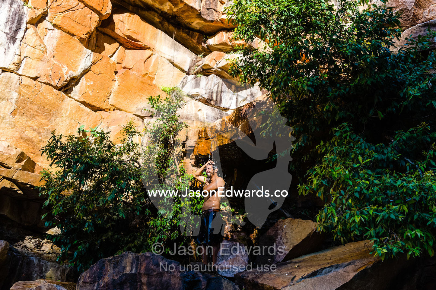 A man takes a cool shower under a small freshwater waterfall in a desert gorge. Calamity Bay, Koolama Bay, Kimberley Coast, Western Australia, Australia.