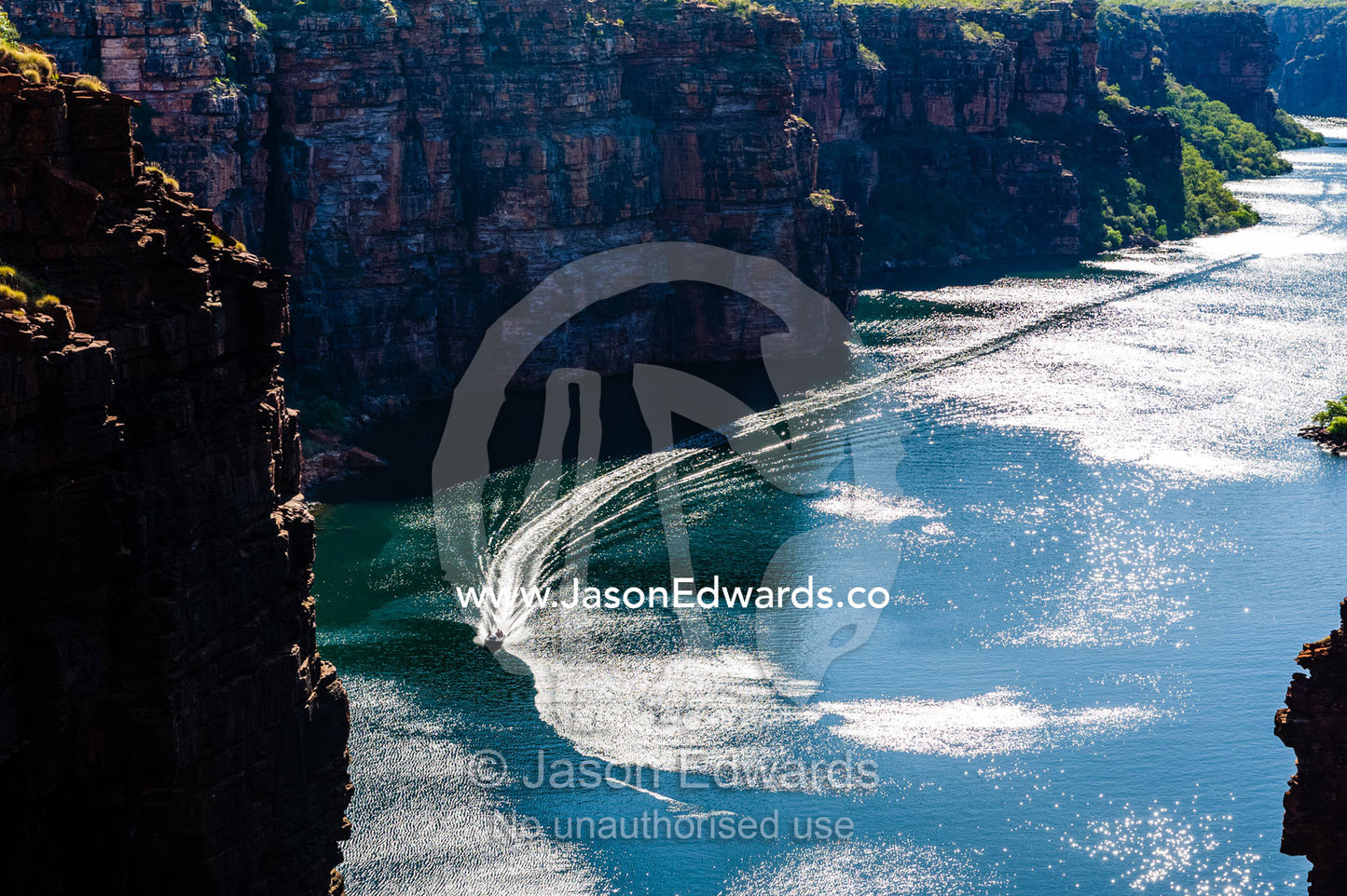A boat cruising along a river beneath sheer cliff walls. King George River, King George Falls, Gardner Plateau, Kimberley Coast, Western Australia, Australia.