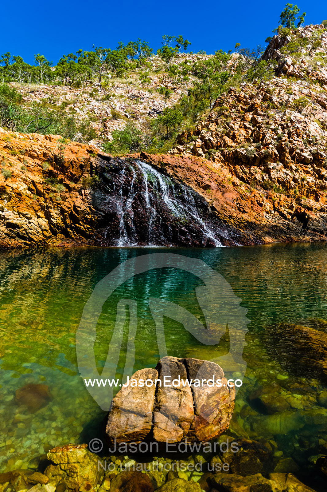 A small waterfall cascades into a sandstone gorge waterhole in the desert. Crocodile Creek, Kimberley Coast, Western Australia, Australia.