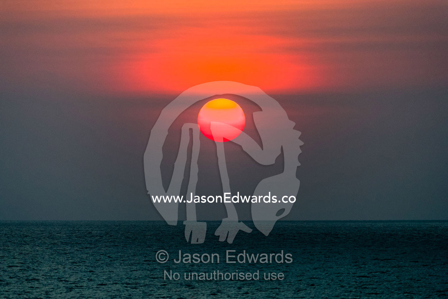 The sun dips into bank of haze above the surface of a tropical ocean. Lava Flow, Banda Neira, Banda Islands, Maluku Province, Indonesia.