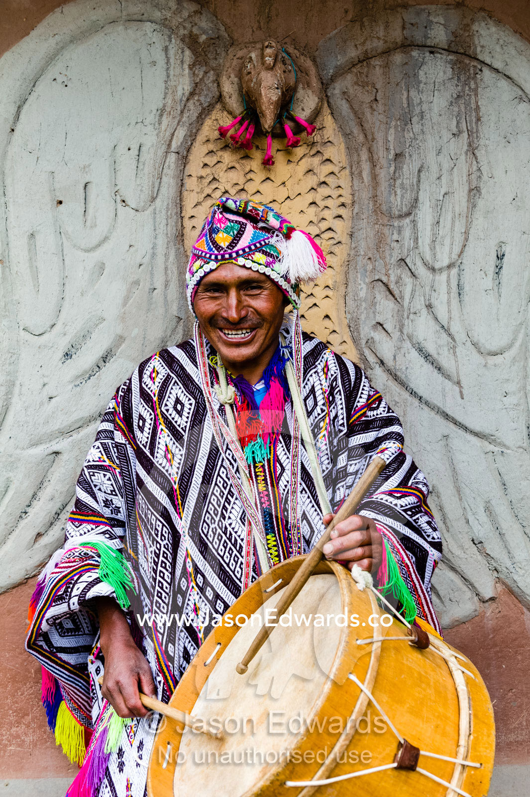 An Amaru man wearing a colorful handwoven poncho and chullo playing a drum. Peru.