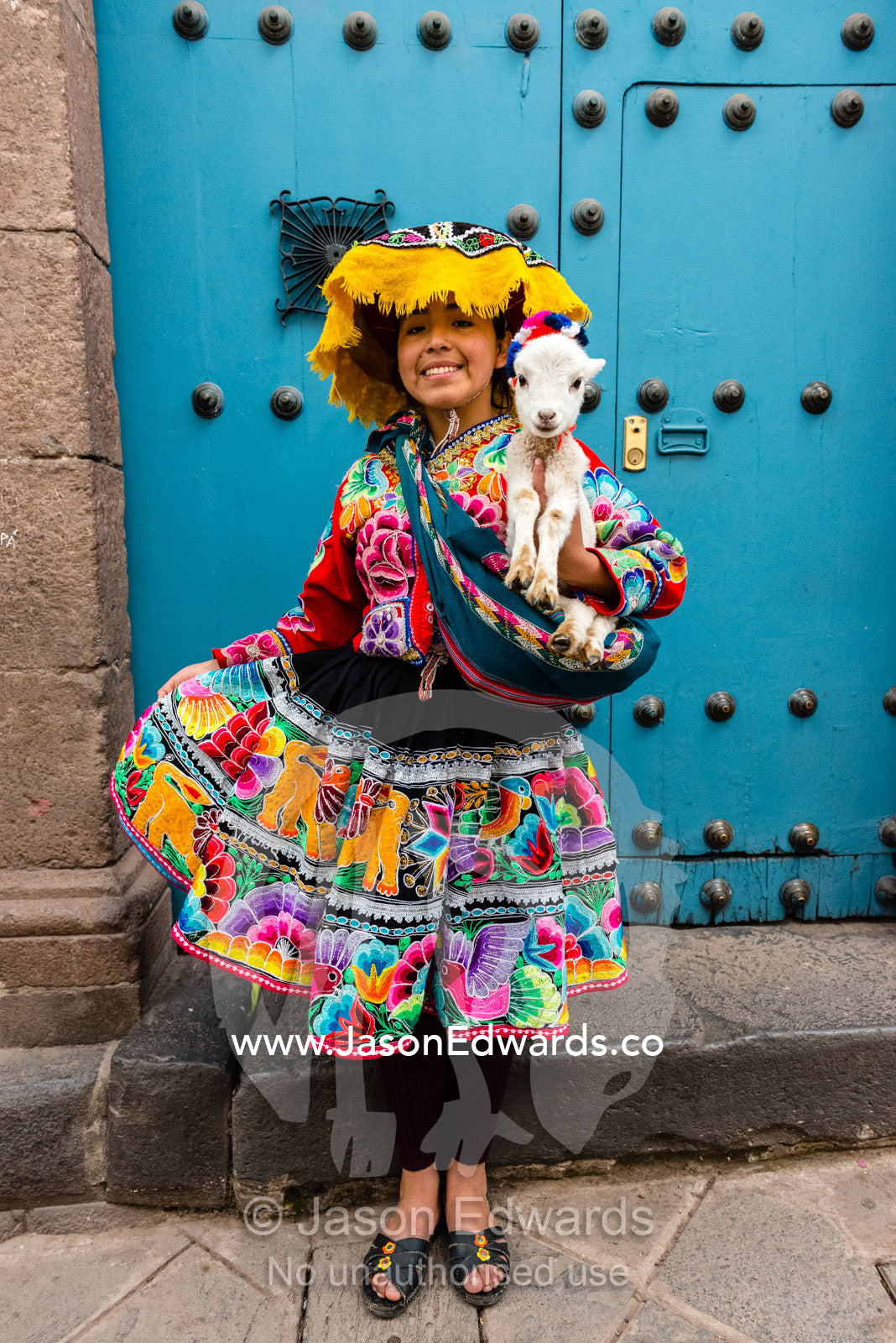 A woman dressed in colorful Montera hat, bayeta and tunic holding a baby lama called a cria. Cusco, Peru.