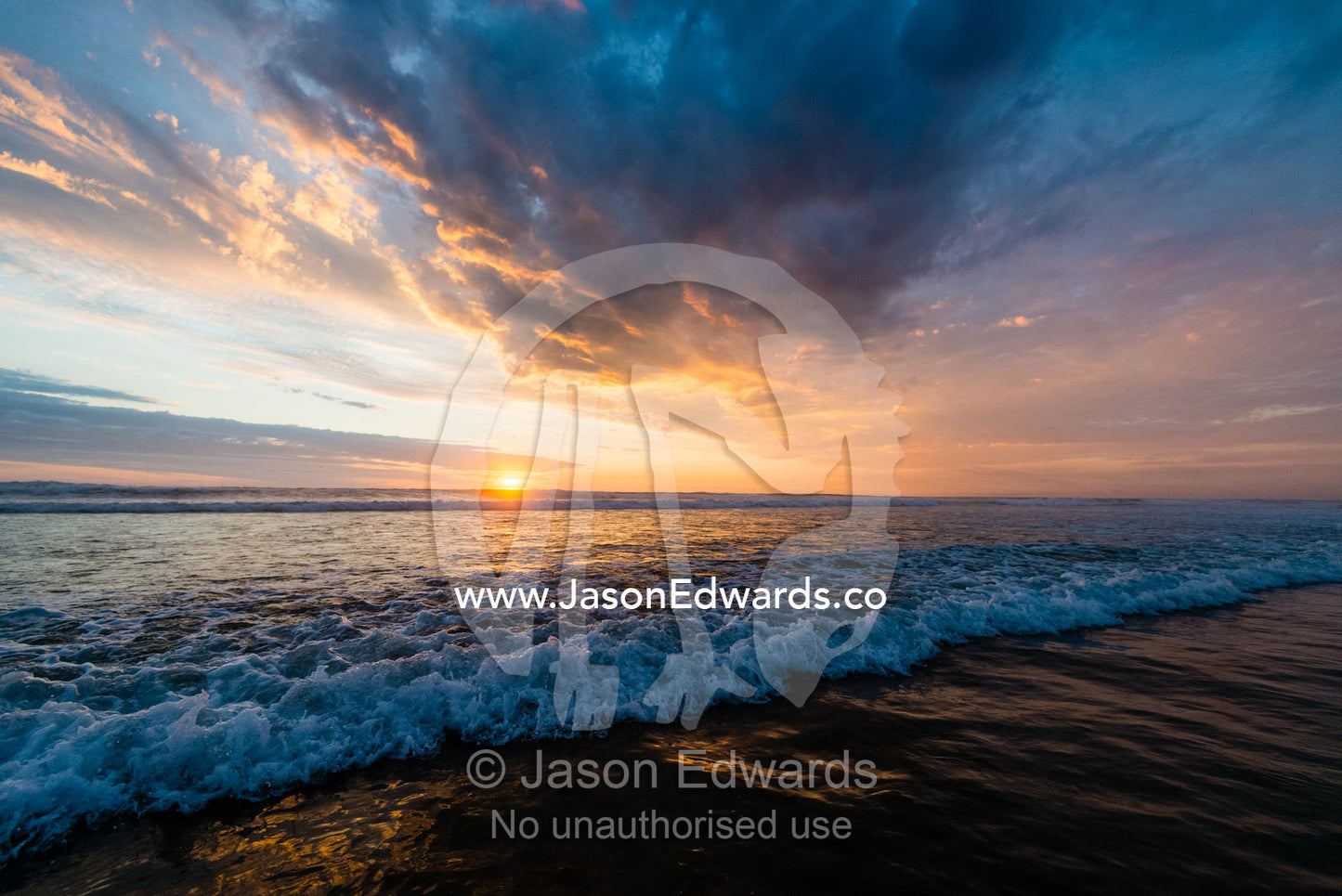 Beneath a storm front an incoming tide pushes waves onto a beach at sunset. Victoria, Australia.