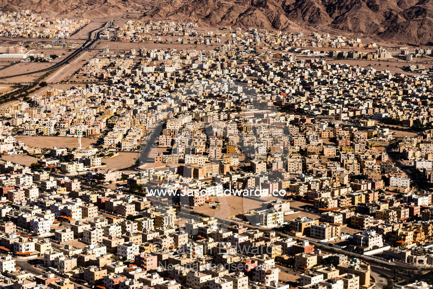 Crowded apartment blocks and housing estates fill a desert valley floor. Amman, Jordan