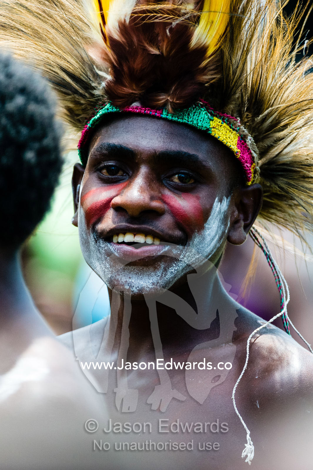 A young Asmat warrior wearing a colorful Bird of Paradise feather headdress during a Bis pole raising ceremony. Syuru Village, Asmat Regency, Papua, Indonesia