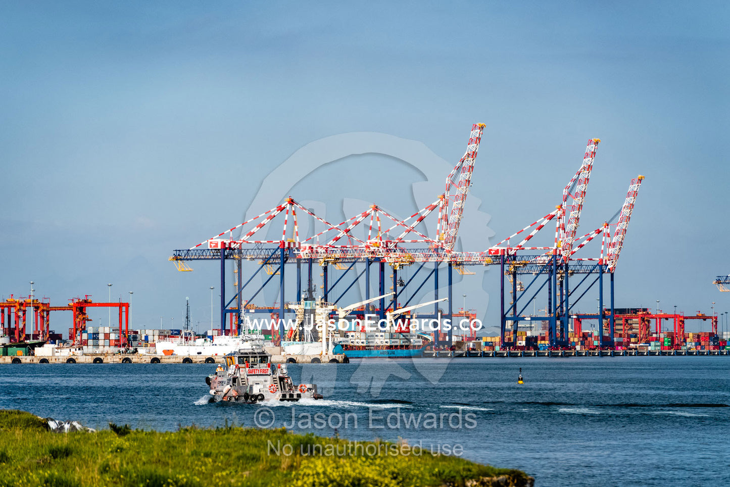 A tug boat sails towards a container ship port and cranes loading cargo for transportation. Cape Town, Western Cape, South Africa