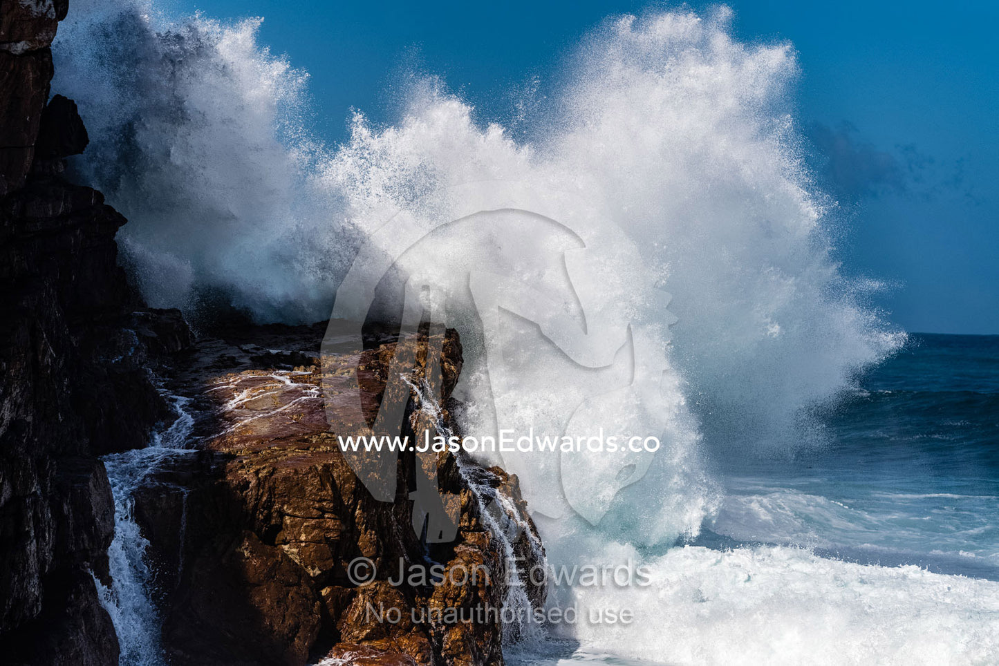 An enormous wave crashes against an ocean cliff sending spray into the air. Cape Point National Park, South Africa