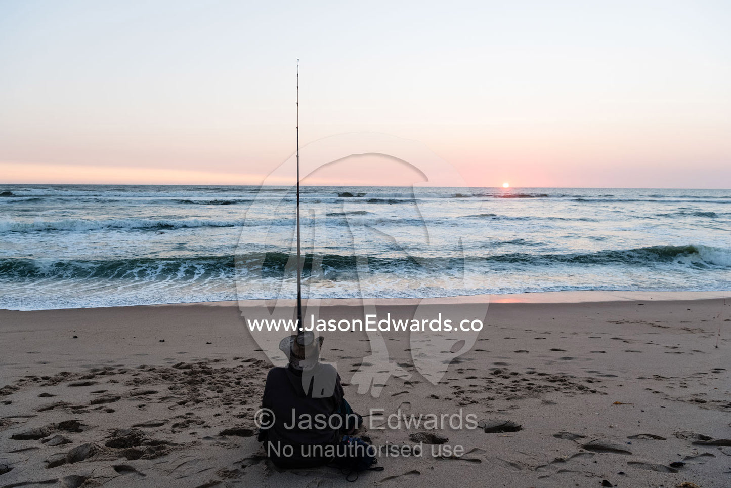A solitary fisherman using a surf fishing rod to catch fish at sunset. Swakopmund, Namibia
