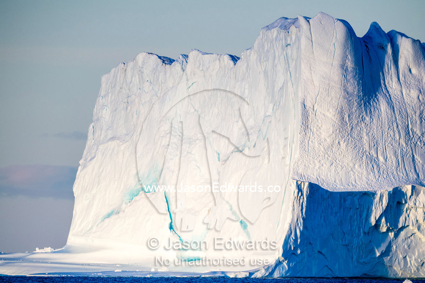 Late afternoon light falls across the surface of sheer iceberg cliffs floating in the arctic. Milne Land, Hall Bredning Fjord, Scoresby Sound, Greenland