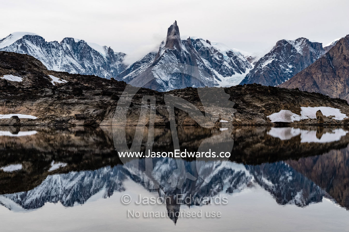 A jagged spire of rock shrouded in ice and snow reflecting in a still arctic pool. O Fjord, Island Fjord, Milne Lan, Grundtvigskirken, Bjorne Islands, Scoresby Sound, Greenland