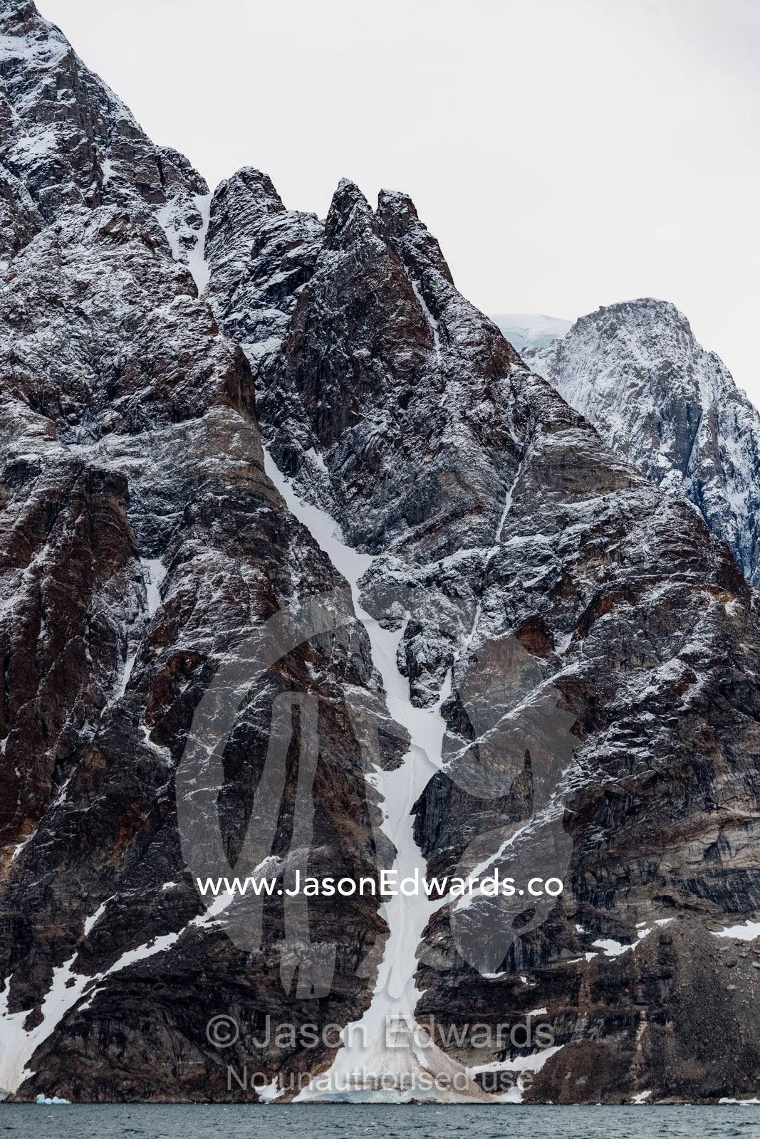 A brutal and sheer cliff face gouged by ice and covered in a dusting of snow. Milne Land, O Fjord, Island Fjord, Scoresby Sound, Greenland