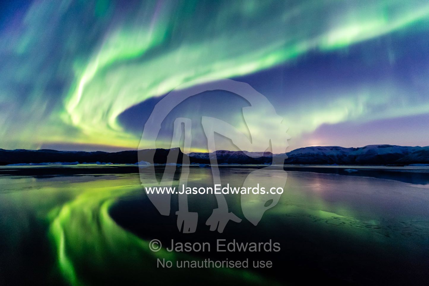 Iridescent green northern lights refecting in the still waters of an arctic fjord at night. Renodde, Rode Fjord, Scoresby Sound, Greenland