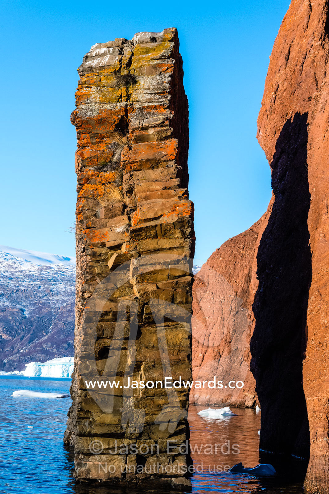 Erosion carves slabs of basalt dykes into pillars beside red conglomerate cliffs in an arctic fjord. Milne Land, Rode Island, Red Island, Rode Fj, Scoresby Sound, Greenland