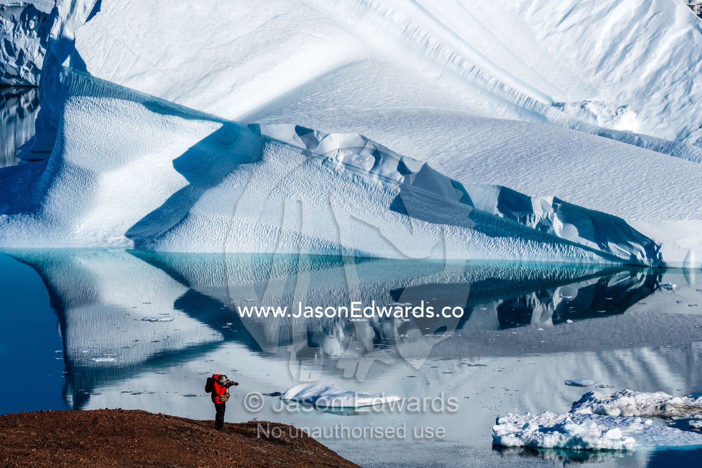 A hiker photographing an Iceberg Graveyard in a fjord. Milne Land, Rode Island, Red Island, Rode Fj, Scoresby Sound, Greenland