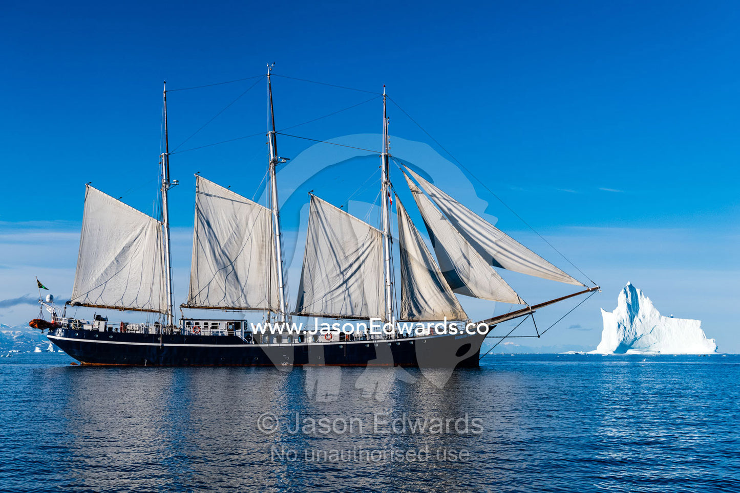 A Tall Ship Schooner sailing past an iceberg in an arctic fjord. Milne Land, Vikingbukt, Viking Bay, Scoresby Sound, Greenland