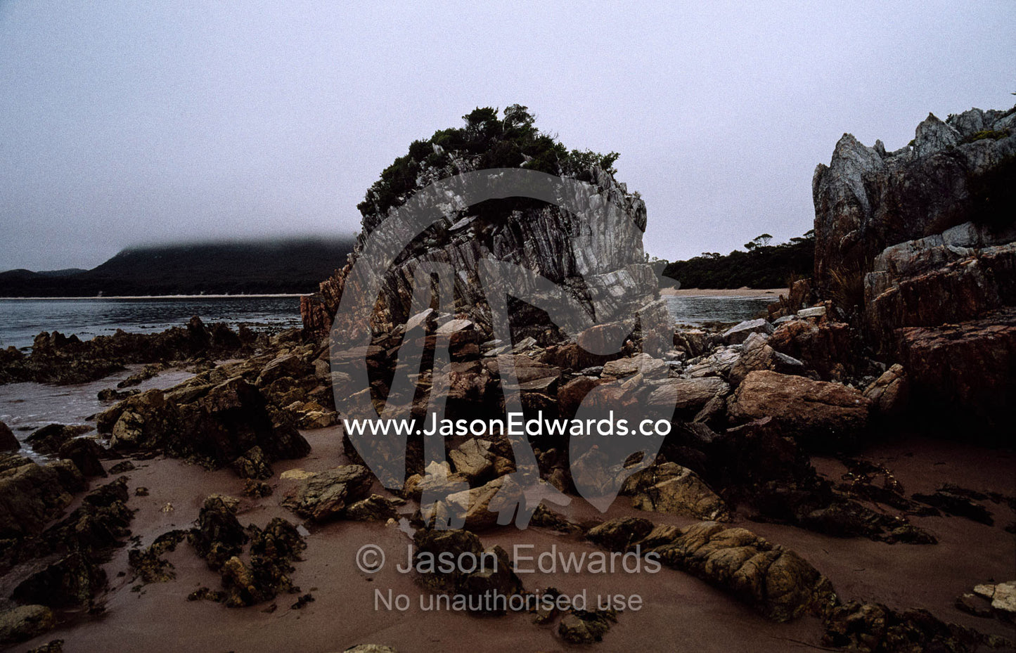 Stormy skies over a granite outcrop exposed at low tide. South West National Park, Tasmanian Wilderness World Heritage Area, Tasmania, Australia.