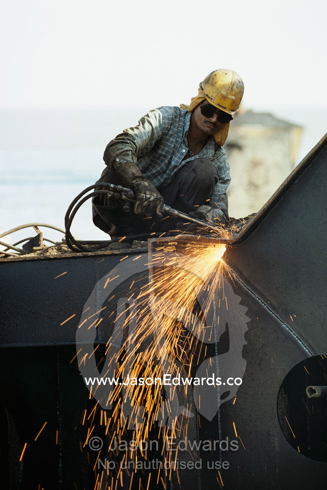 A worker cuts apart an old ship to reclaim the steel for recycling. Alang, India.