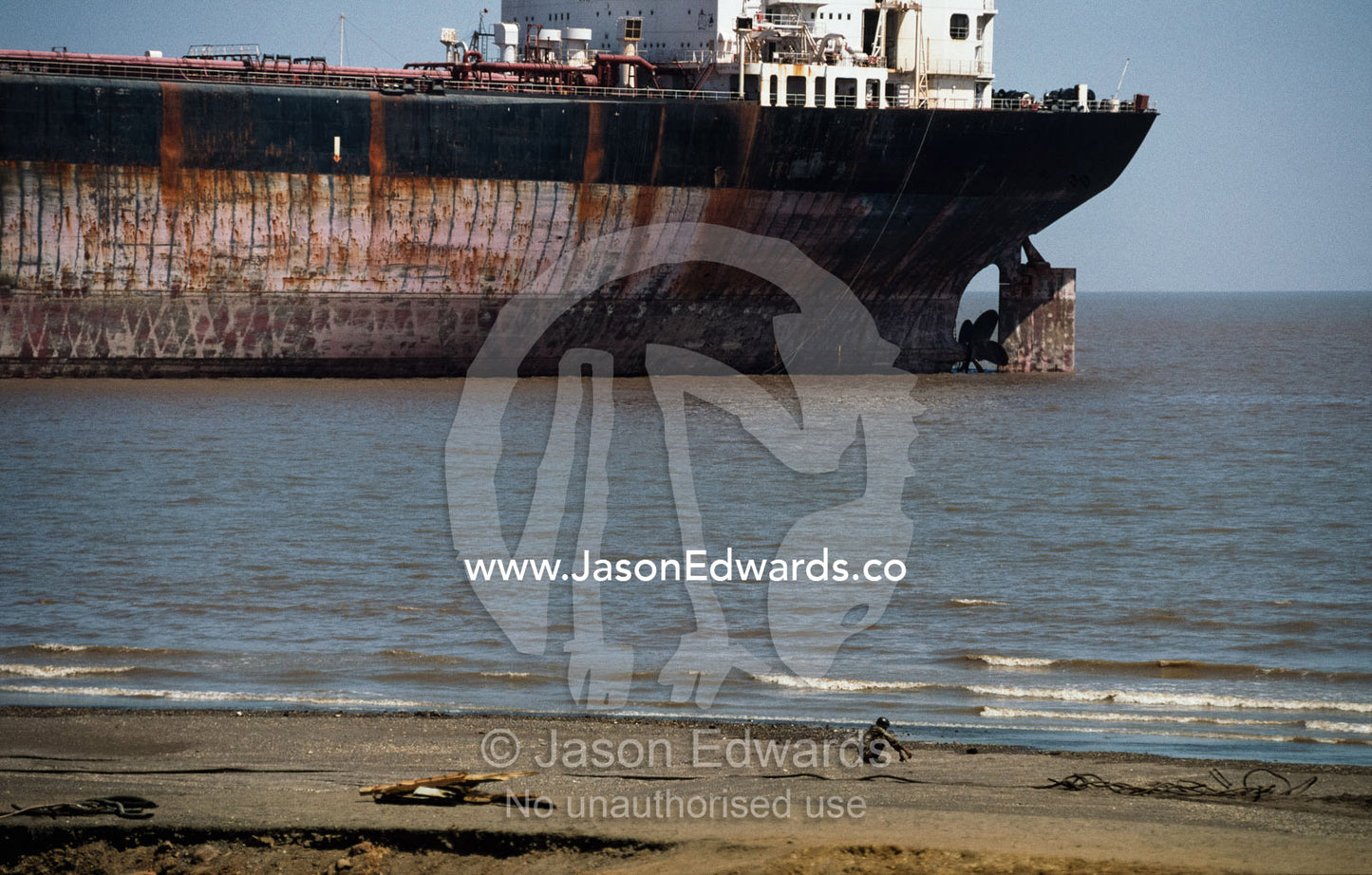 A tanker dwarfs a laborer huddled on the beach. Alang, India.
