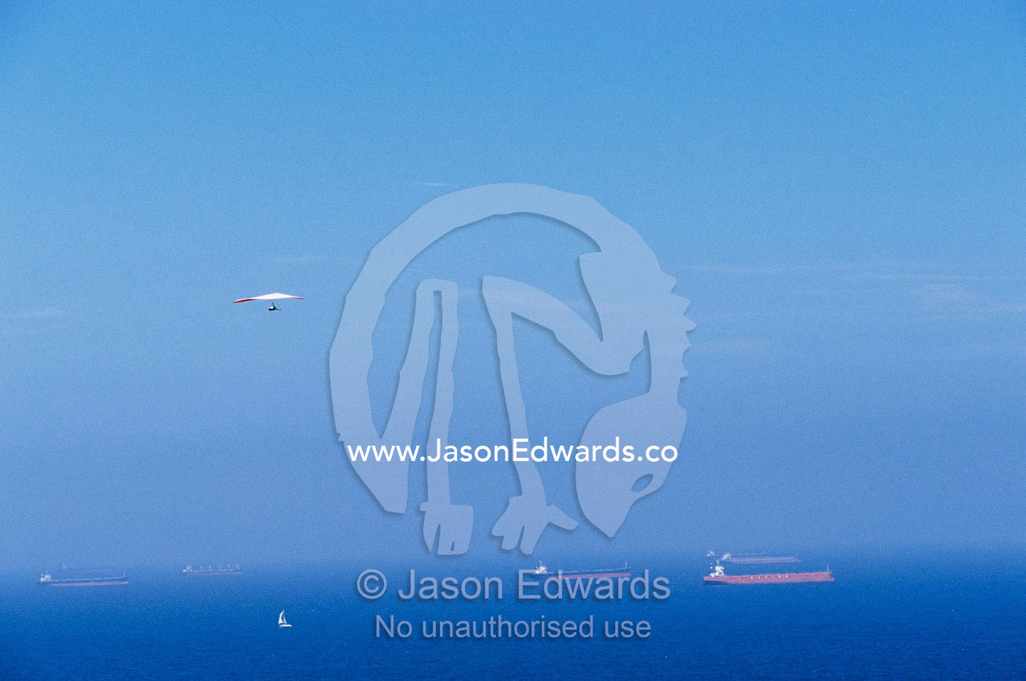 A hang glider in blue sky over a sea dotted with ships and boats. Merewether, New South Wales, Australia.