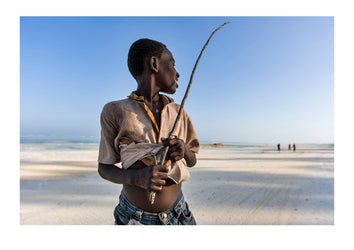 A young boy herding his family cattle along a deserted beach is distracted by the calls from his young siblings and the reprimands of his father. Zanzibar.