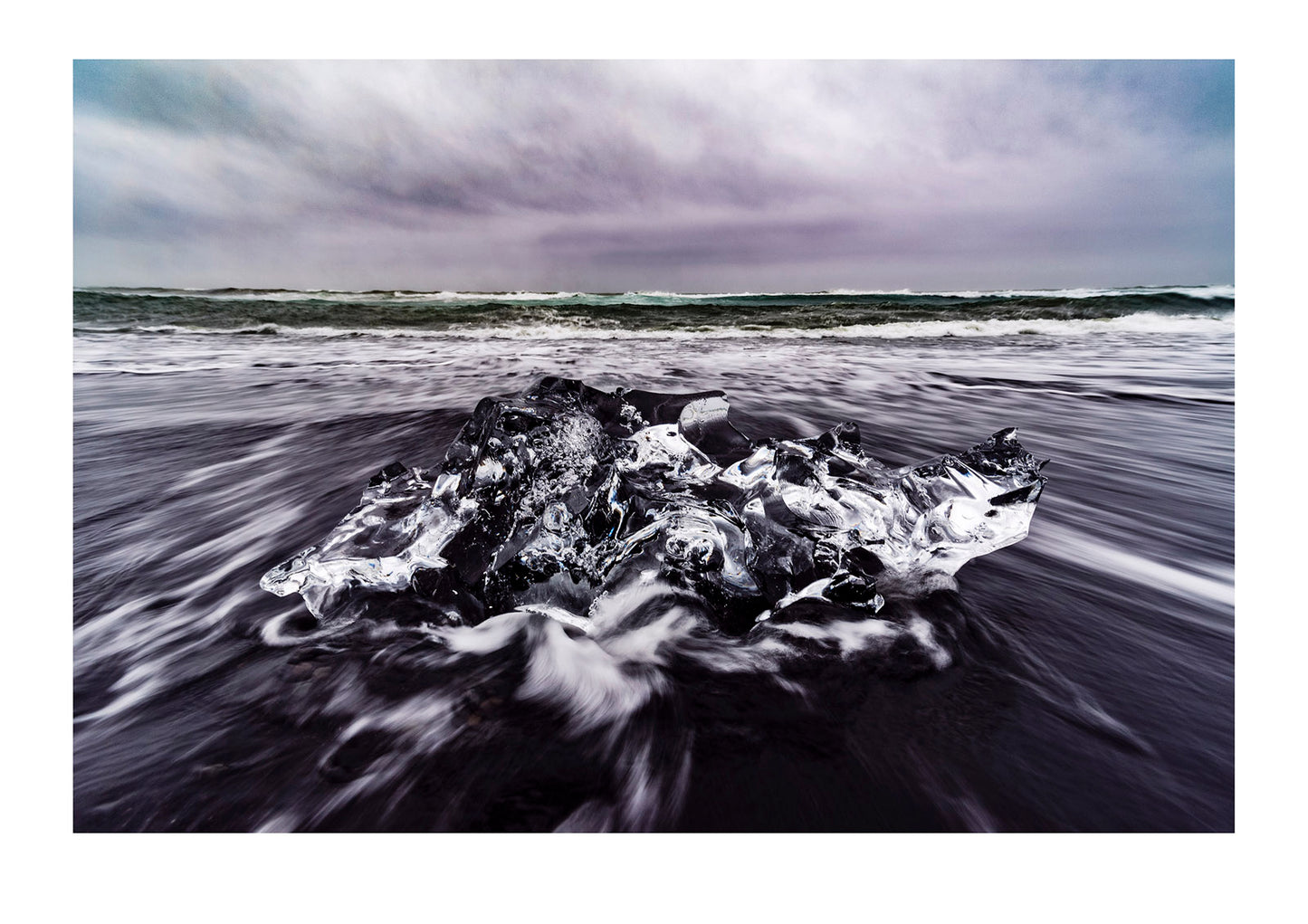 A raging sea casts waves onto a black volcanic sand beach and glacier iceberg. Iceland.
