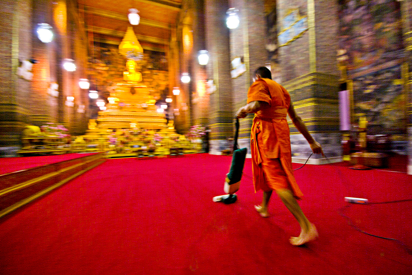 A Buddhist Monk vacuums the chapel's red carpet after evening prayer. Wat Pho, Temple of the Reclining Buddha, Wat Chetuphon, Phra Nakhon District, Rattanakosin District, Bangkok, Thailand.