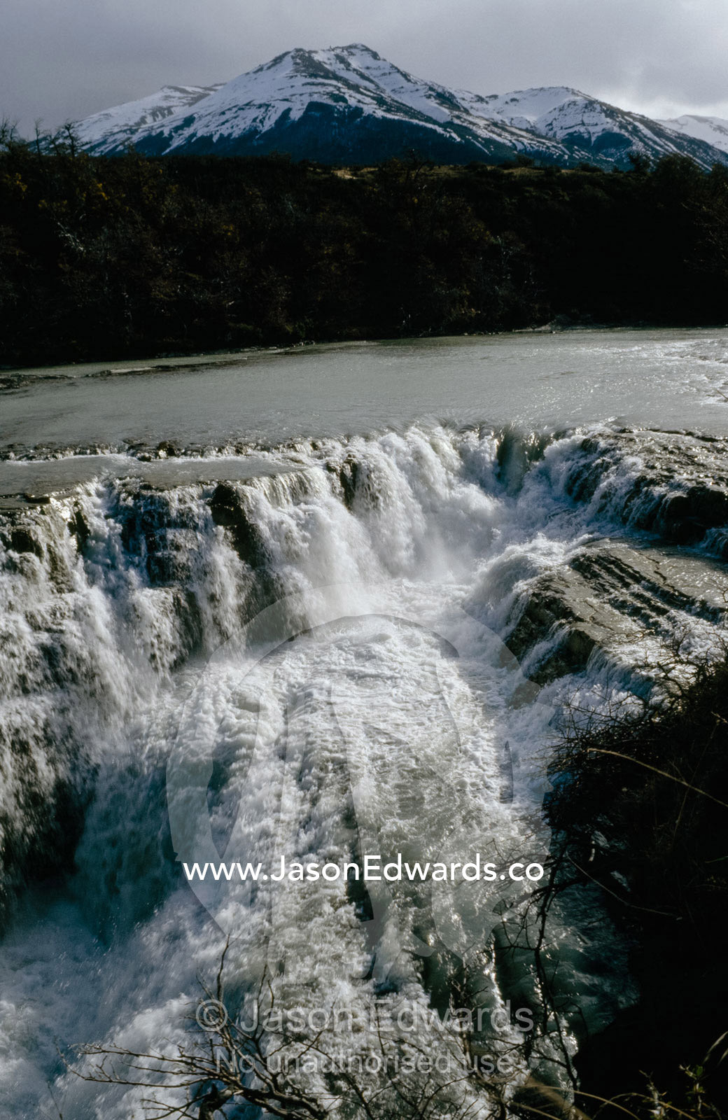 A cascading waterfall with a snow and ice-covered mountain backdrop.   Torres del Paine National Park, Chile.