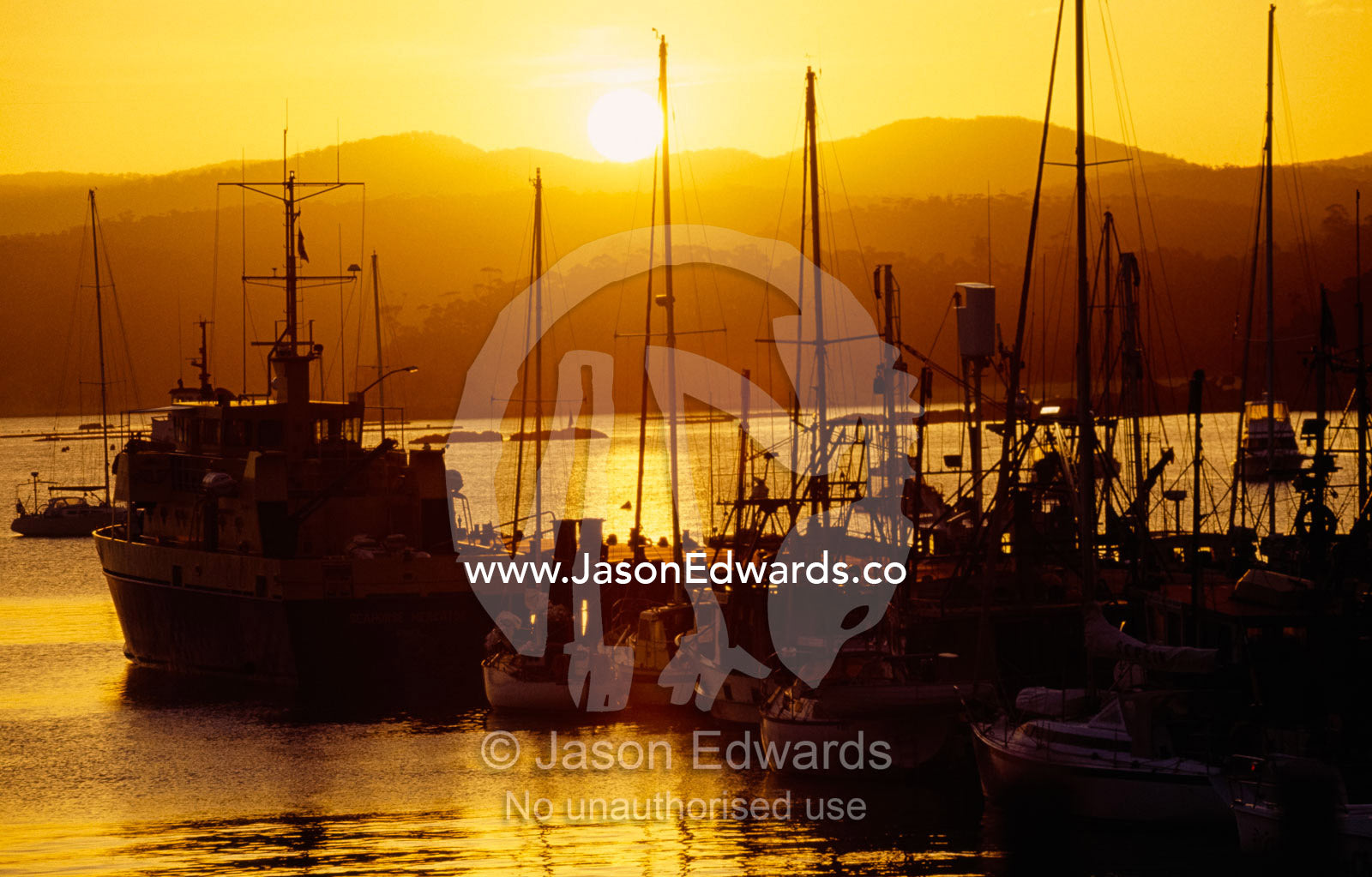 Moored yachts at a pier silhouetted by the setting sun. Eden, New South Wales, Australia.
