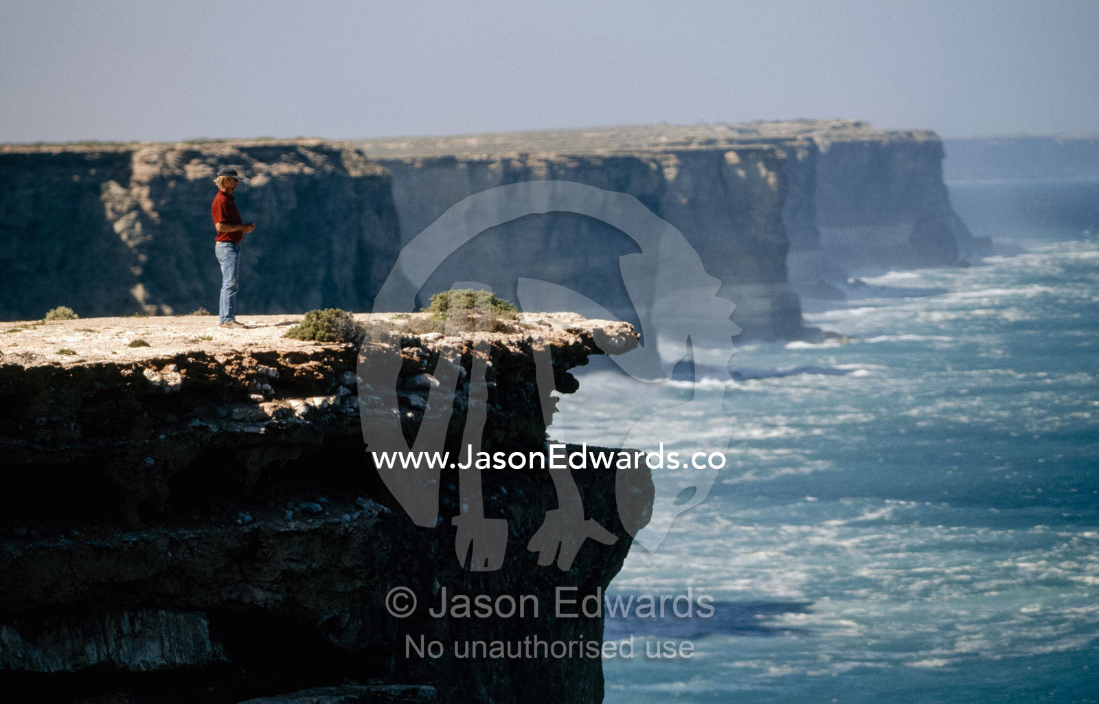 A tourist guide stands on the edge of a cliff high above the ocean. Head of the Bight, South Australia.