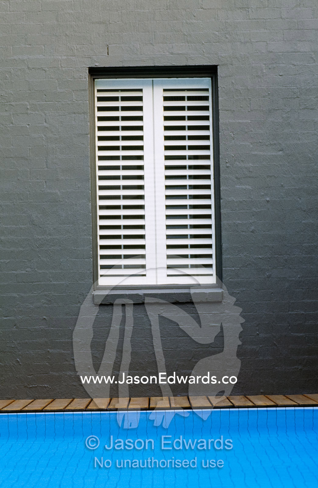 A shuttered window overlooking a blue swimming pool and wooden deck. Warrandyte, Victoria, Australia.