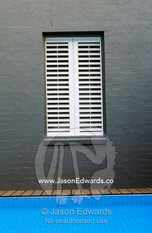 A shuttered window overlooking a blue swimming pool and wooden deck. Warrandyte, Victoria, Australia.