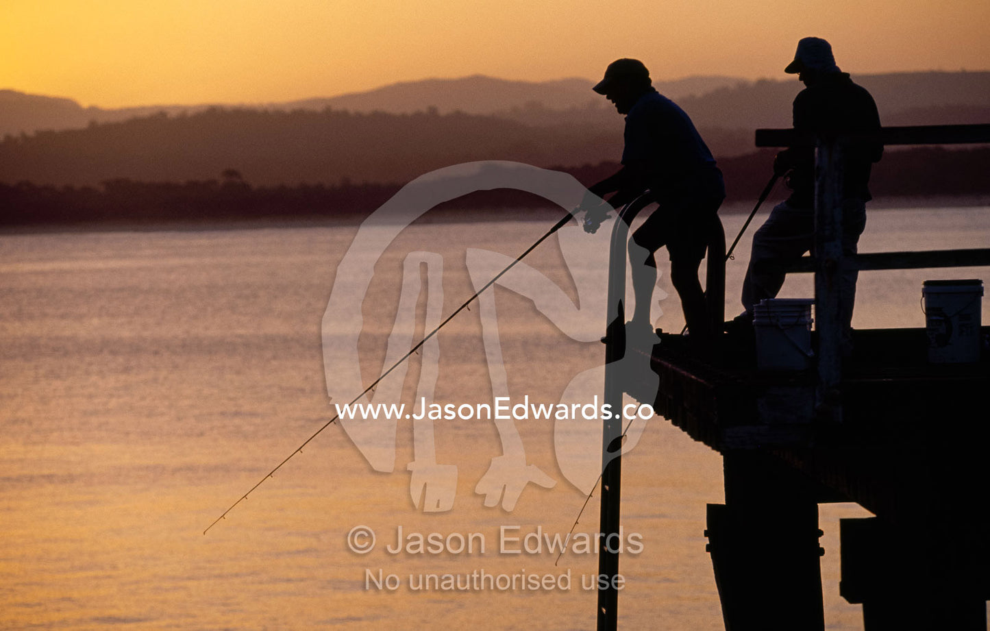 Silhouetted fishermen on Merimbula Wharf at sunset. Merimbula, New South Wales, Australia.