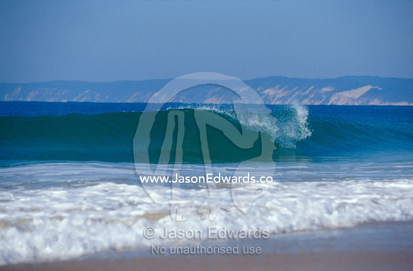Waves break on a pristine sandy beach with cliffs in the background. Great Sandy National Park, Cooloola, Fraser Island, Queensland, Australia.