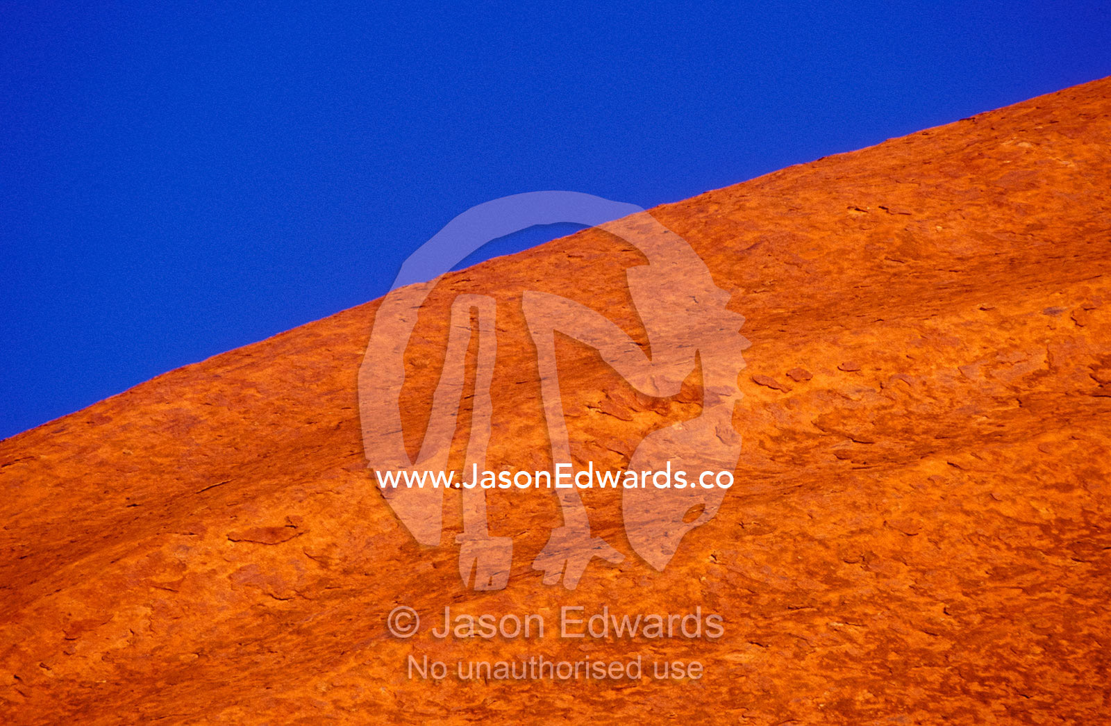 A crested dome of Uluru also known as Ayers Rock red under a blue sky. Uluru-Kata Tjuta National Park, Northern Territory, Australia
