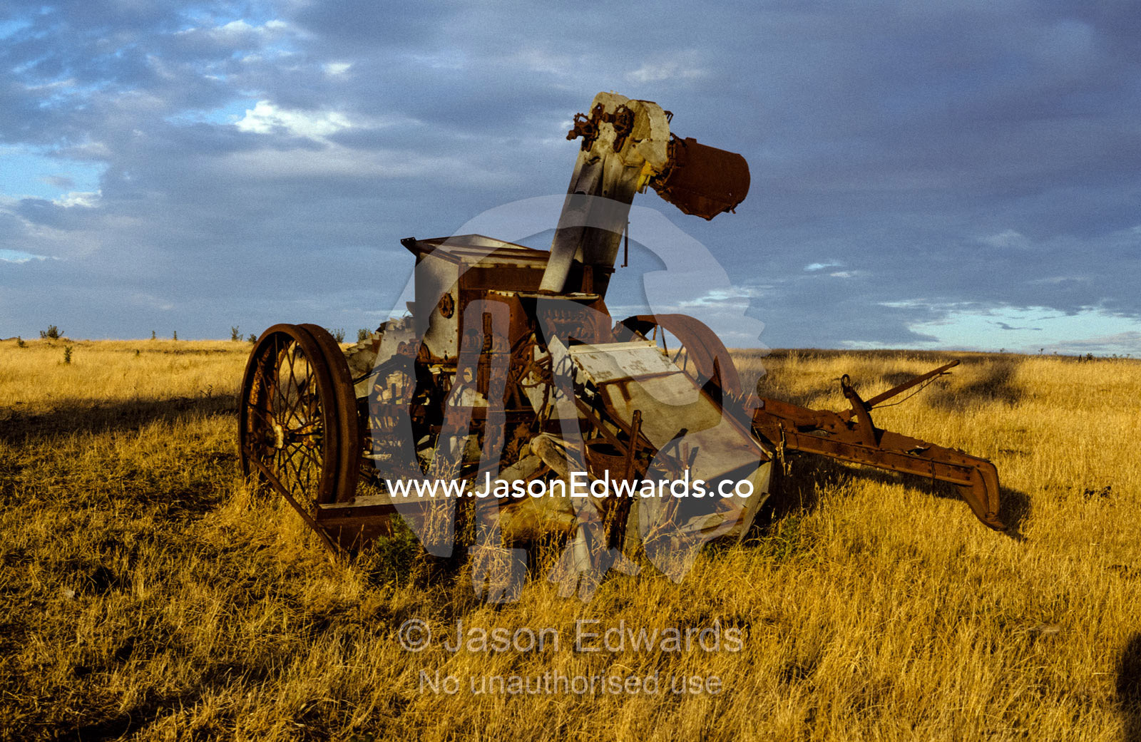 Discarded antique farm harvester machinery rusting in a field at dawn. near Bendigo, Victoria, Australia.