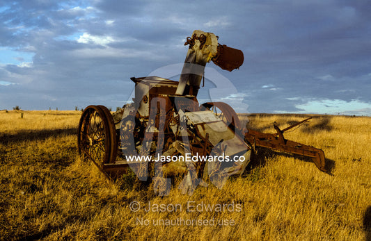 Discarded antique farm harvester machinery rusting in a field at dawn. near Bendigo, Victoria, Australia.
