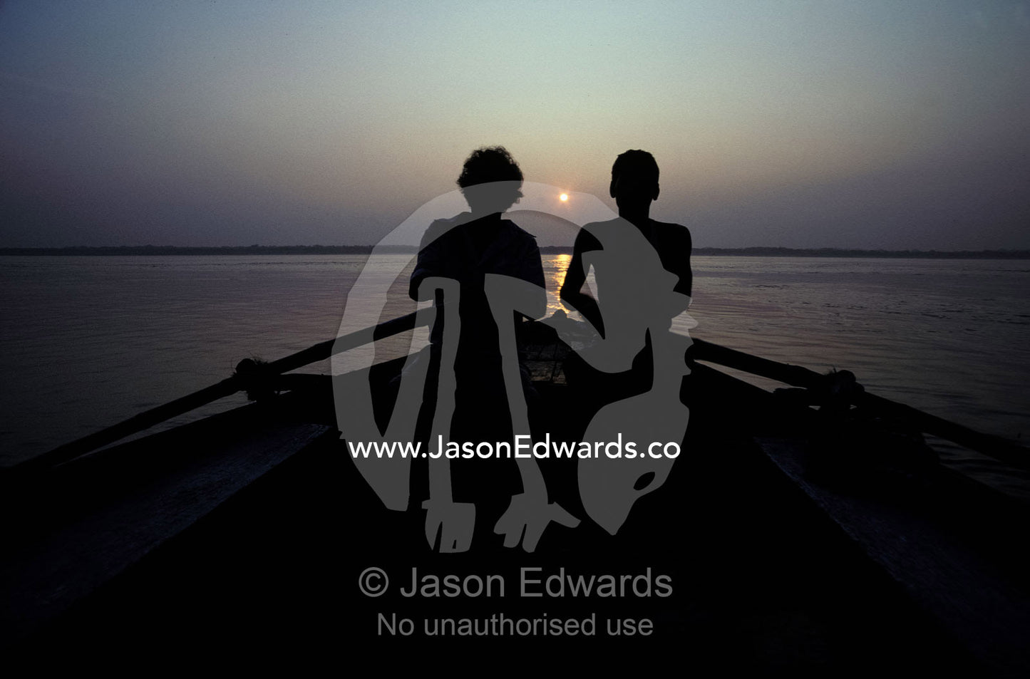 Silhouettes of boatmen rowing at dawn on the holy Ganges River. Ganges River, Varanassi, India.