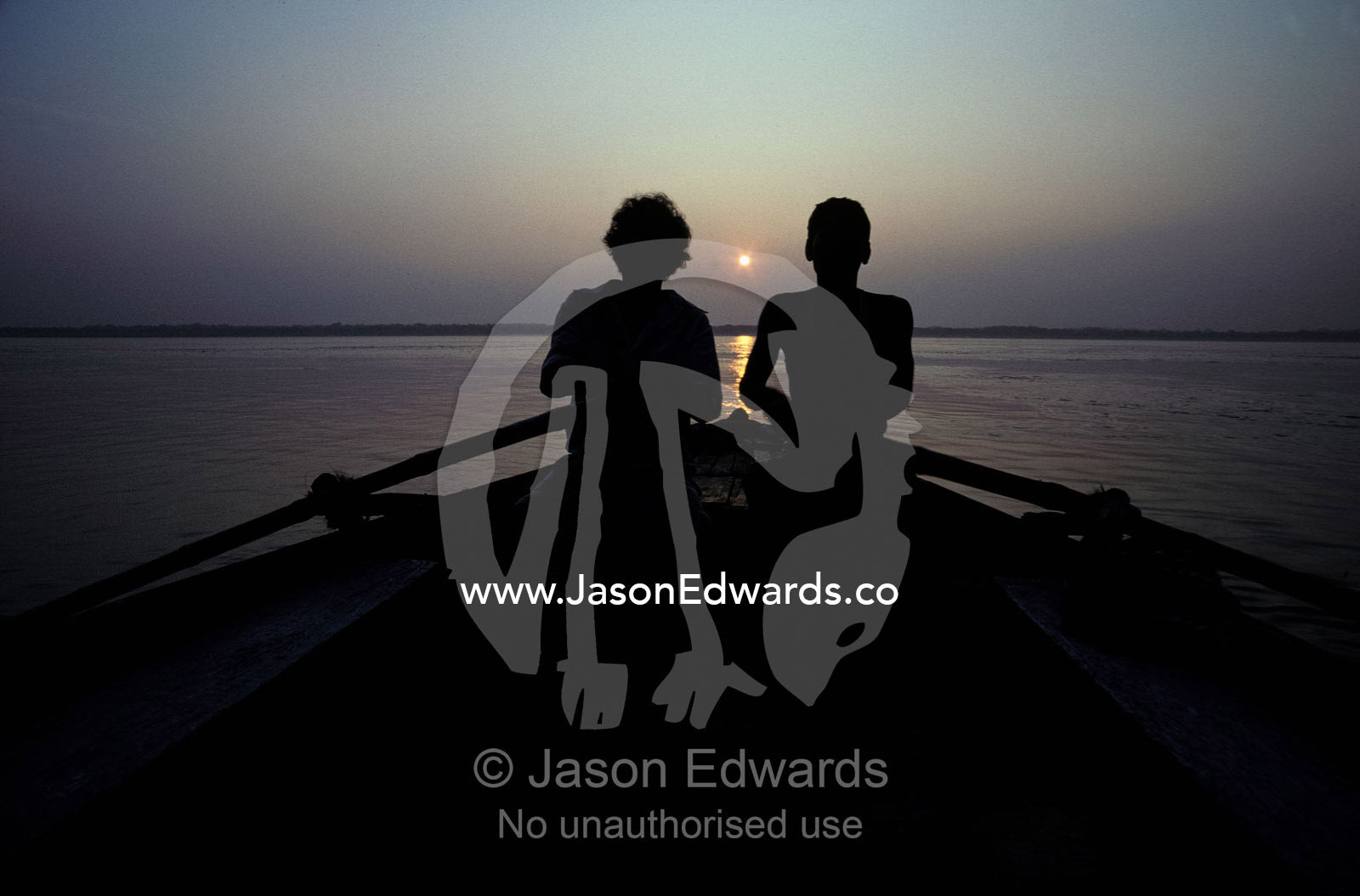 Silhouettes of boatmen rowing at dawn on the holy Ganges River. Ganges River, Varanassi, India.