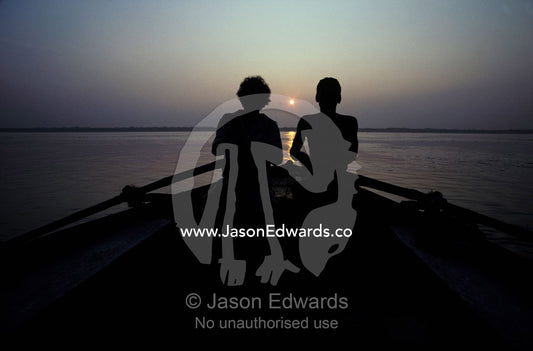 Silhouettes of boatmen rowing at dawn on the holy Ganges River. Ganges River, Varanassi, India.