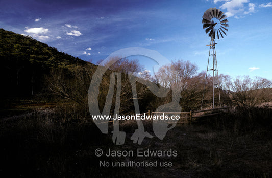 A windmill situated alongside a river in a field in late winter. Howqua River, Victoria Australia